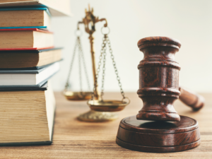 A stack of law books, a scale of justice and a gavel on a desk.