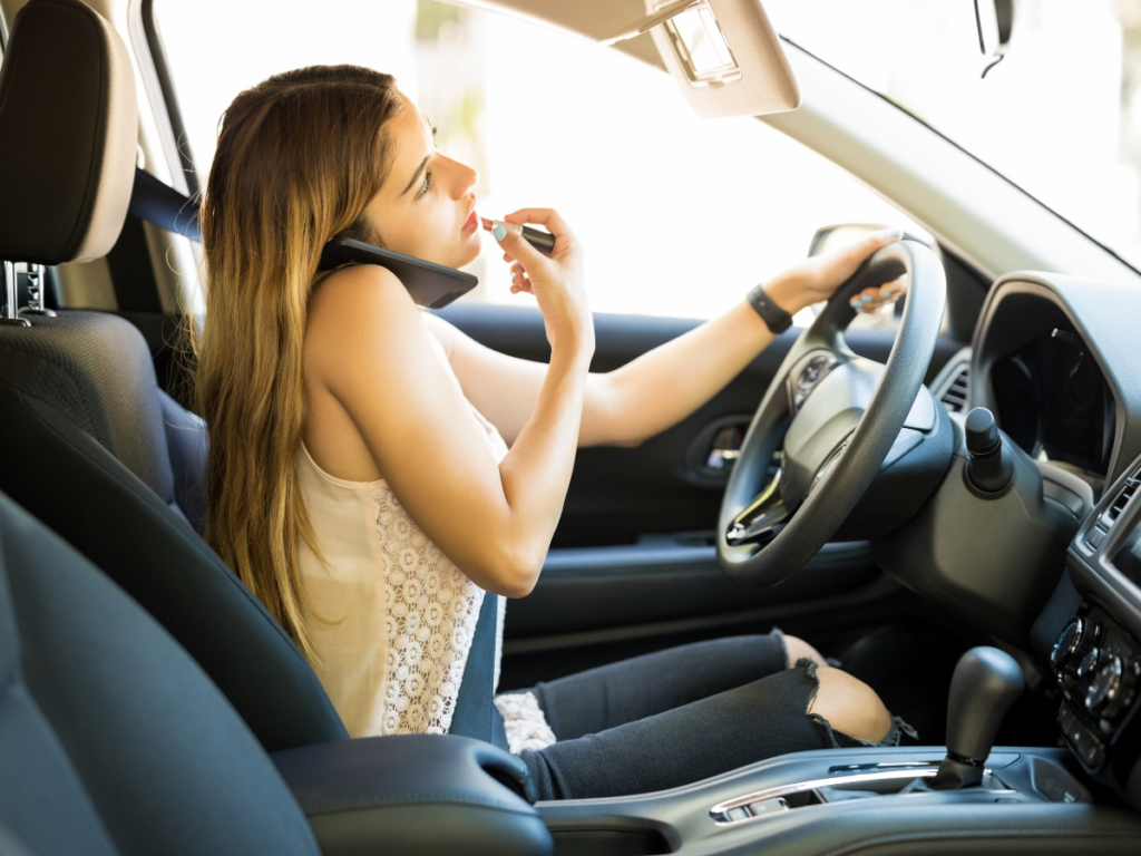 A woman driving on the phone and putting on lipstick.
