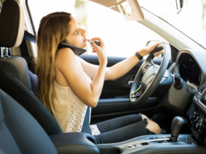 A woman driving on the phone and putting on lipstick.