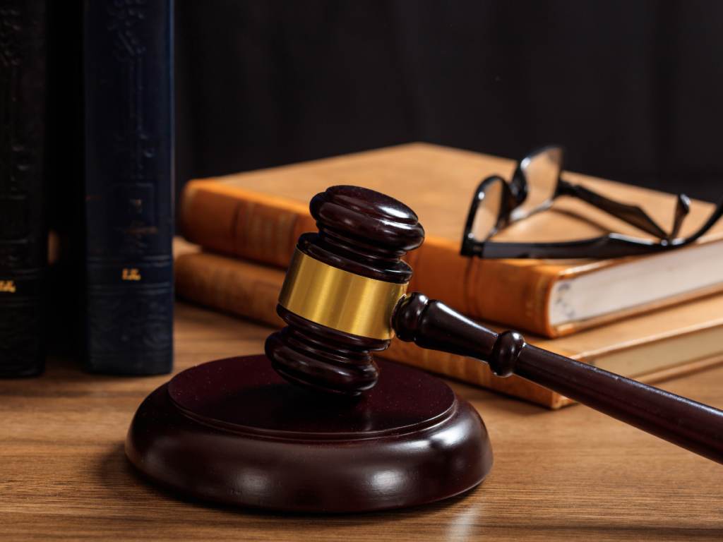A judges gavel on a table with a lawbook and glasses.