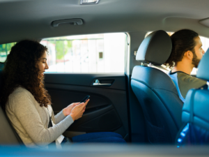A woman in the back seat of an uber/lyft with a driver in front.